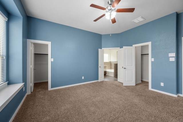 unfurnished bedroom with ensuite bathroom, a walk in closet, carpet floors, and ceiling fan