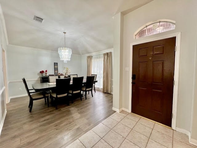 entrance foyer featuring light hardwood / wood-style flooring, ornamental molding, and a notable chandelier