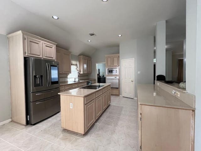 kitchen with vaulted ceiling, appliances with stainless steel finishes, a kitchen island, and light brown cabinets