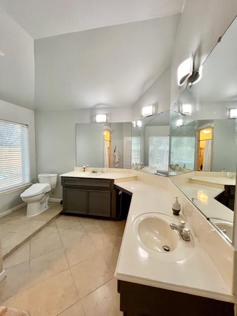 bathroom featuring toilet, tile patterned flooring, vaulted ceiling, vanity, and walk in shower