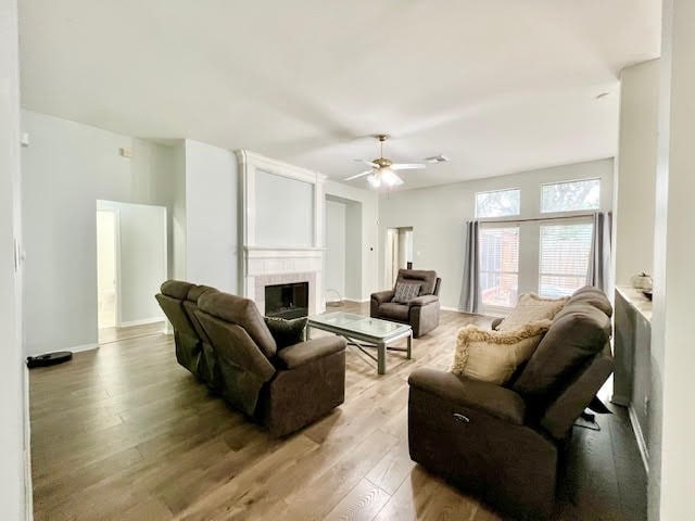 living room featuring a tiled fireplace, light wood-type flooring, and ceiling fan