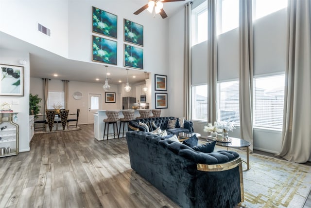 living room with light hardwood / wood-style floors, a towering ceiling, plenty of natural light, and ceiling fan