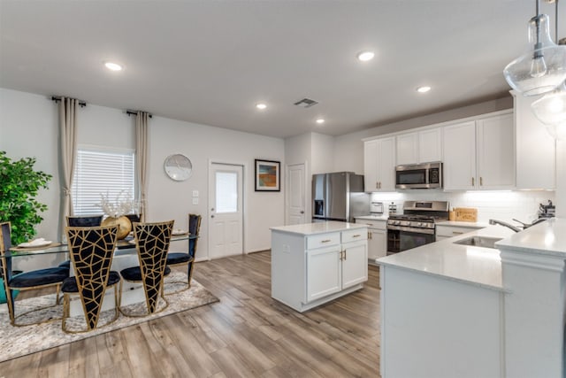 kitchen featuring white cabinets, hanging light fixtures, light hardwood / wood-style flooring, sink, and stainless steel appliances