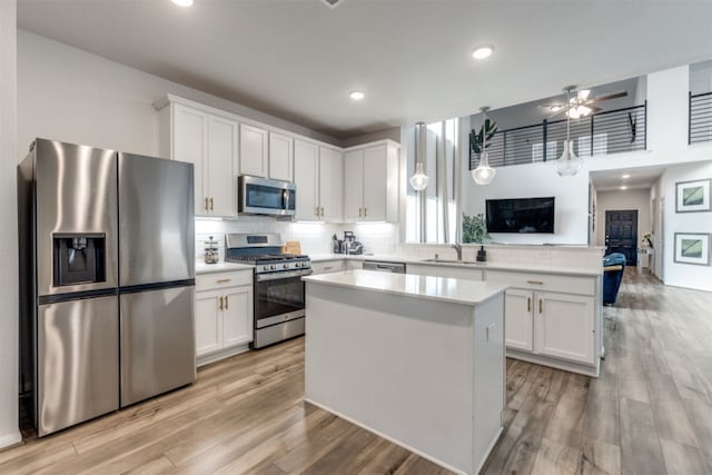 kitchen with appliances with stainless steel finishes, light wood-type flooring, a kitchen island, white cabinetry, and ceiling fan