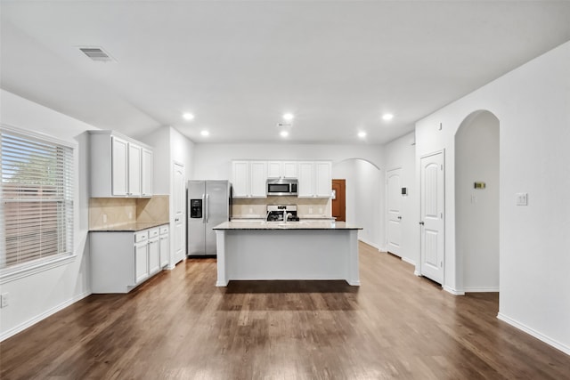 kitchen with appliances with stainless steel finishes, dark hardwood / wood-style flooring, an island with sink, and white cabinets