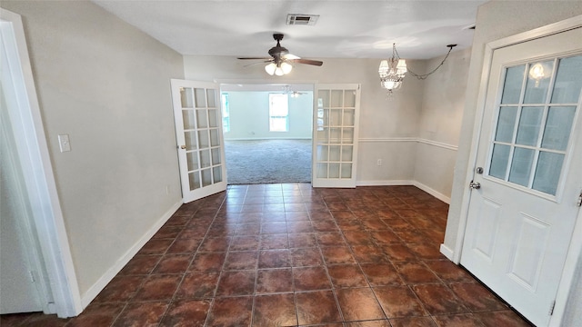 unfurnished dining area featuring french doors, dark colored carpet, and ceiling fan with notable chandelier