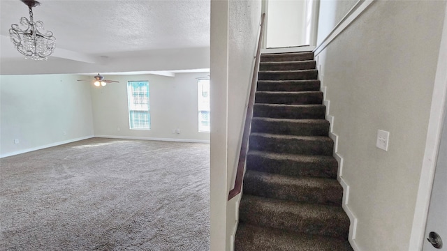 stairs with a textured ceiling, carpet floors, and ceiling fan with notable chandelier