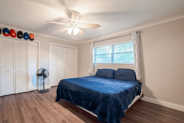 bedroom with two closets, ceiling fan, a textured ceiling, ornamental molding, and dark hardwood / wood-style floors