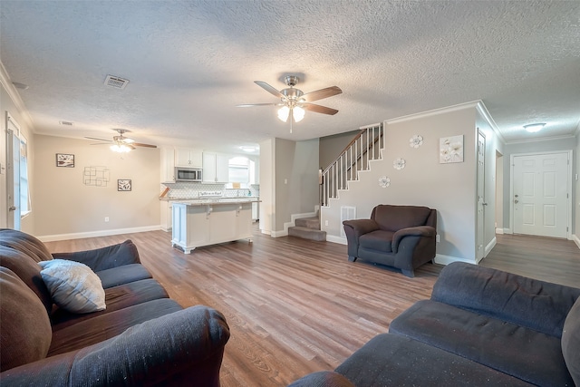 living room featuring ornamental molding, a textured ceiling, light wood-type flooring, and ceiling fan