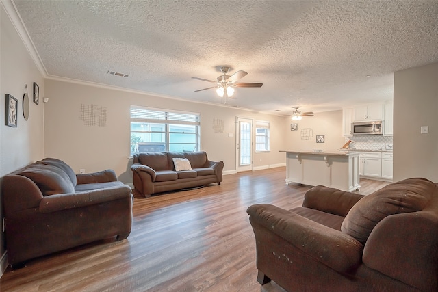 living room with light hardwood / wood-style floors, crown molding, a textured ceiling, and ceiling fan