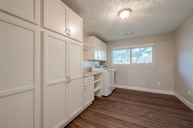 laundry room featuring dark hardwood / wood-style flooring, a textured ceiling, washing machine and clothes dryer, and cabinets