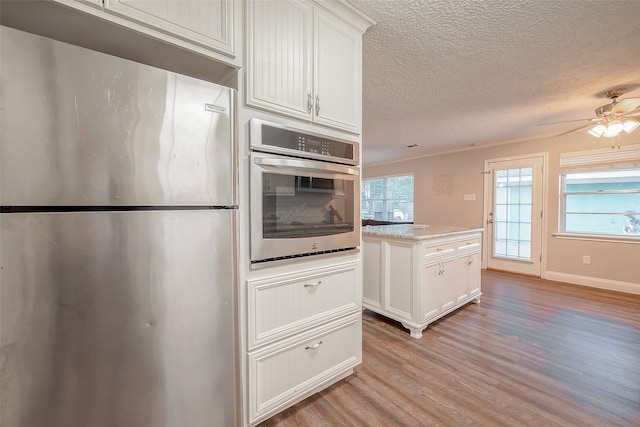 kitchen with a wealth of natural light, appliances with stainless steel finishes, white cabinetry, and light wood-type flooring