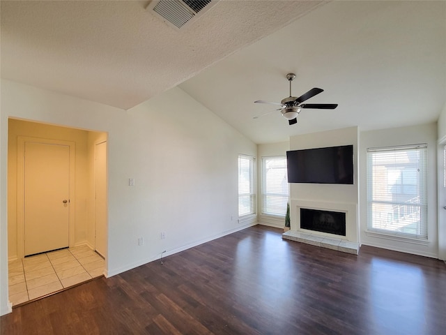 unfurnished living room featuring lofted ceiling, visible vents, a glass covered fireplace, ceiling fan, and wood finished floors