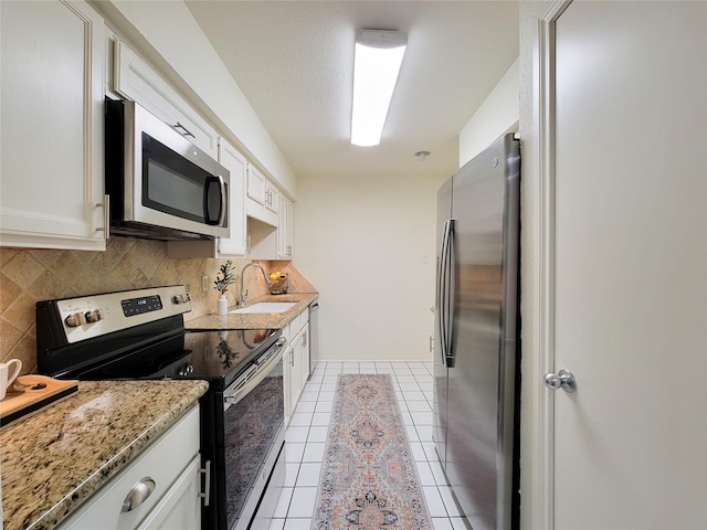 kitchen with light stone counters, stainless steel appliances, a sink, white cabinets, and tasteful backsplash