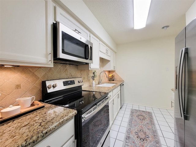 kitchen with appliances with stainless steel finishes, a sink, light stone counters, and white cabinets