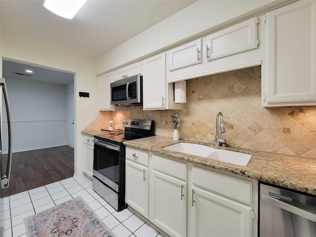 kitchen with light tile patterned floors, a sink, white cabinetry, appliances with stainless steel finishes, and light stone countertops