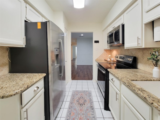 kitchen with stainless steel appliances, light stone countertops, white cabinetry, and light tile patterned floors