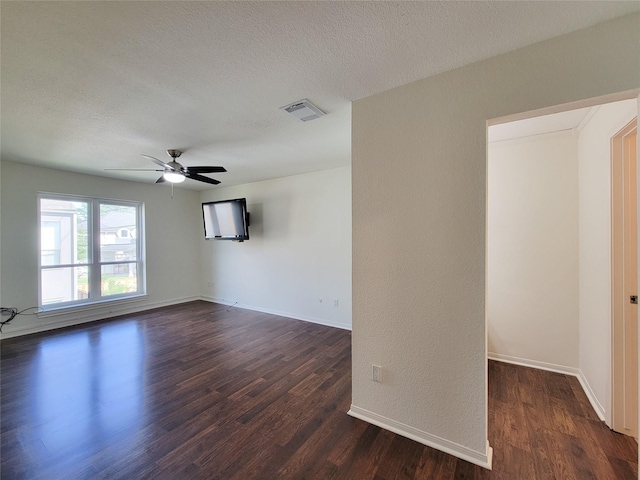 empty room with a textured ceiling, dark wood finished floors, visible vents, and baseboards