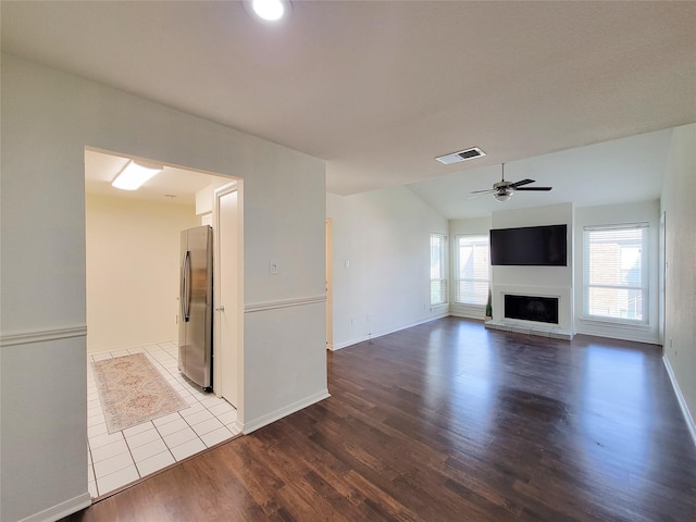 unfurnished living room with vaulted ceiling, a ceiling fan, a fireplace with raised hearth, visible vents, and wood finished floors