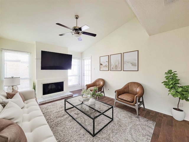 living area featuring ceiling fan, a glass covered fireplace, vaulted ceiling, and wood finished floors