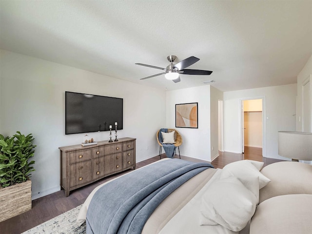 bedroom with dark wood-type flooring, visible vents, baseboards, a ceiling fan, and a walk in closet