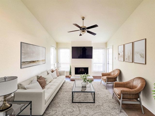 living room featuring vaulted ceiling, a fireplace with raised hearth, ceiling fan, and plenty of natural light