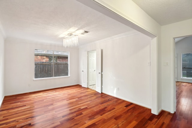 empty room featuring ornamental molding, hardwood / wood-style floors, a textured ceiling, and an inviting chandelier