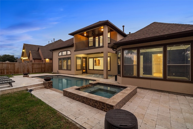 back house at dusk with a balcony, a swimming pool with hot tub, and a patio area