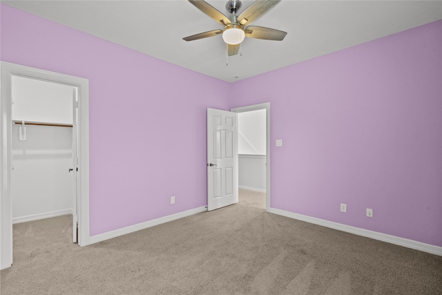 unfurnished bedroom with a closet, ceiling fan, light carpet, and a walk in closet