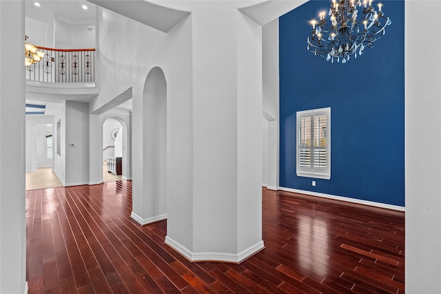 hallway with dark wood-type flooring, a towering ceiling, and an inviting chandelier