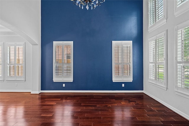 spare room with a towering ceiling, a chandelier, and dark hardwood / wood-style floors