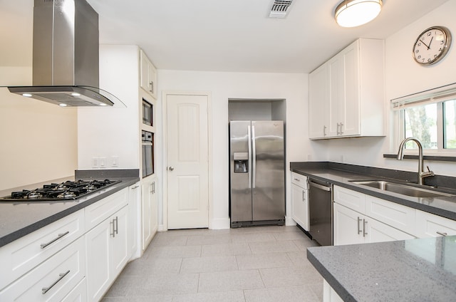 kitchen featuring wall chimney range hood, white cabinets, dark stone counters, sink, and stainless steel appliances