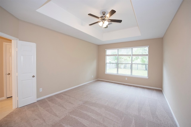 carpeted empty room featuring ceiling fan and a raised ceiling