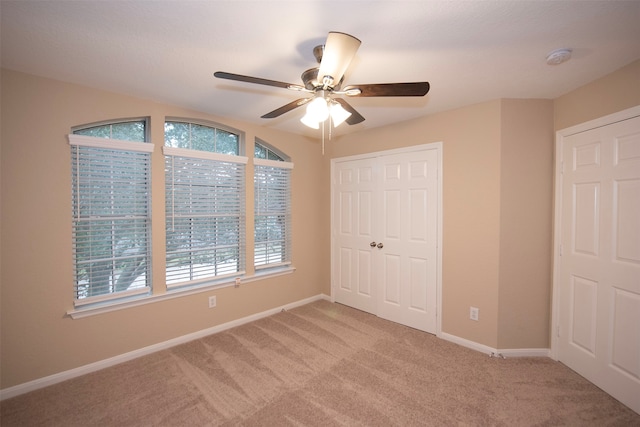 unfurnished bedroom featuring light carpet, multiple windows, a closet, and ceiling fan