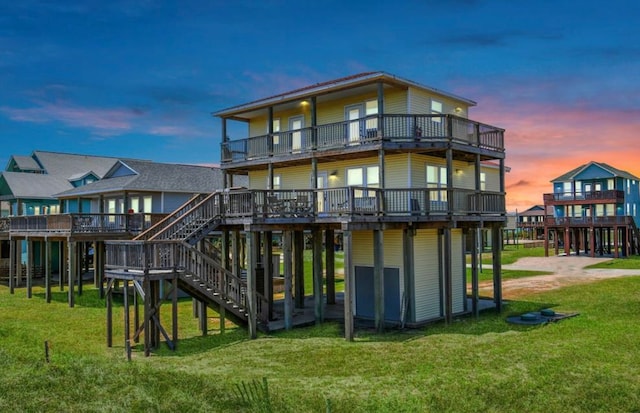 back house at dusk featuring a balcony, a deck, and a lawn