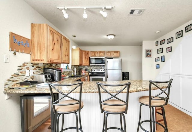 kitchen with kitchen peninsula, decorative backsplash, a kitchen breakfast bar, a textured ceiling, and stainless steel appliances