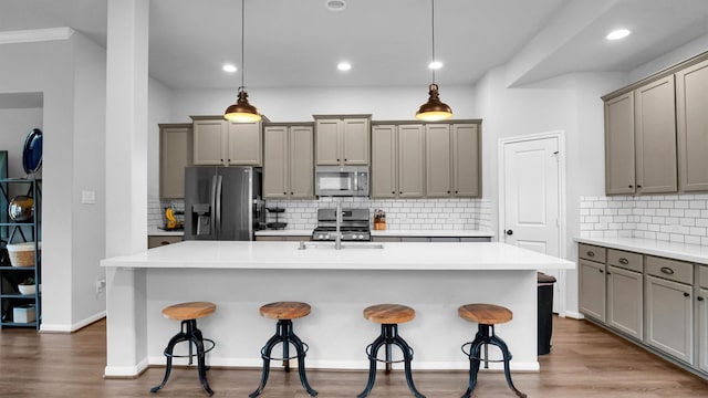 kitchen with a center island with sink, hardwood / wood-style floors, pendant lighting, appliances with stainless steel finishes, and tasteful backsplash