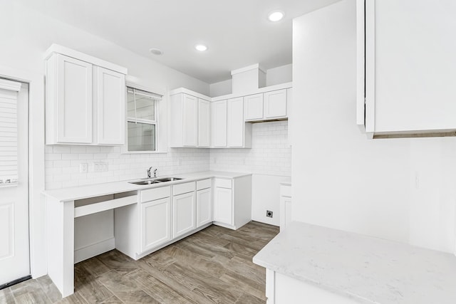 kitchen with light stone countertops, tasteful backsplash, sink, light hardwood / wood-style flooring, and white cabinets