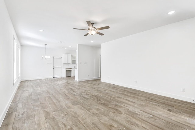 unfurnished living room with ceiling fan with notable chandelier and light wood-type flooring