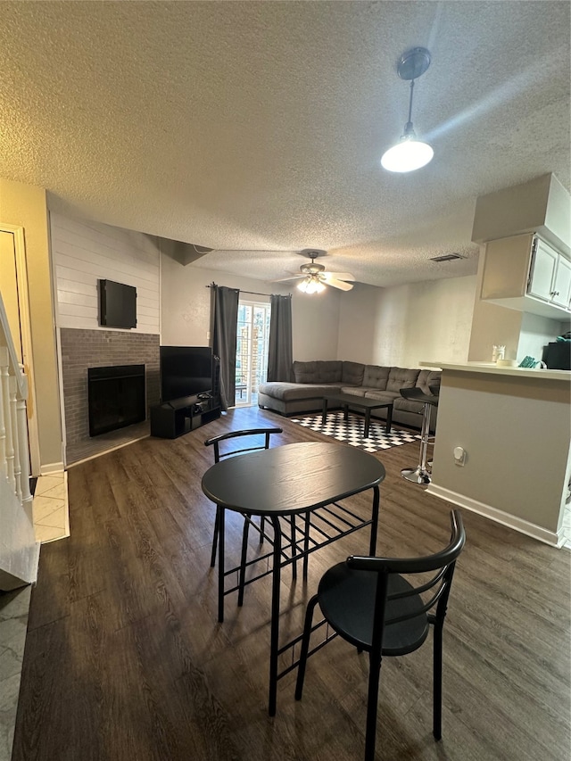 dining area featuring a textured ceiling, a large fireplace, dark wood-type flooring, and ceiling fan