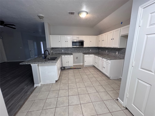 kitchen featuring white cabinets, kitchen peninsula, tasteful backsplash, and dark stone countertops