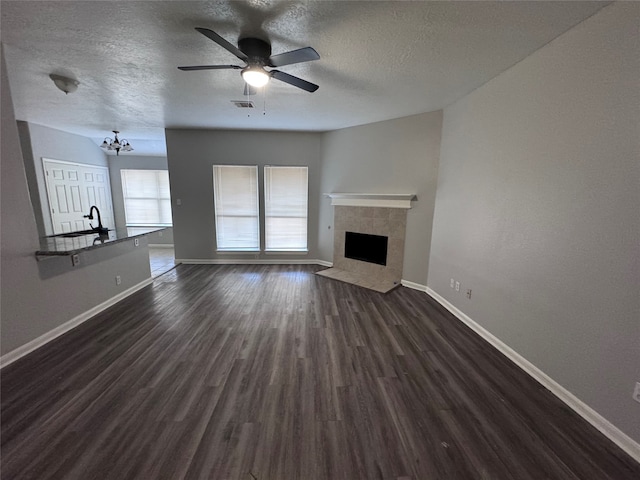 unfurnished living room featuring a tiled fireplace, sink, a textured ceiling, ceiling fan with notable chandelier, and dark hardwood / wood-style flooring