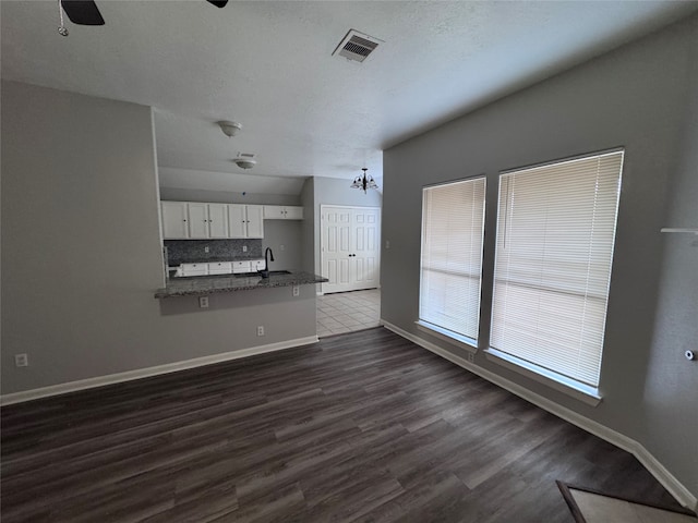 unfurnished living room featuring vaulted ceiling, ceiling fan with notable chandelier, and dark hardwood / wood-style flooring