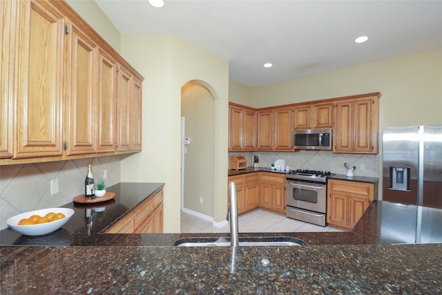 kitchen featuring light tile patterned flooring, sink, appliances with stainless steel finishes, tasteful backsplash, and dark stone counters