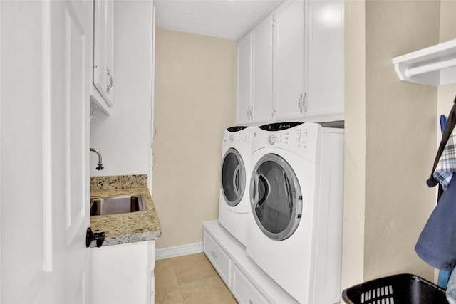 clothes washing area with sink, cabinets, a textured ceiling, washer and clothes dryer, and light tile patterned flooring