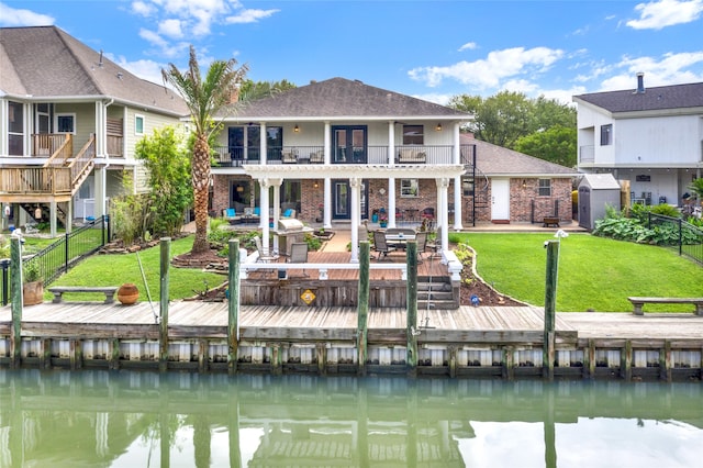 rear view of property with a lawn, a balcony, a deck with water view, and a patio