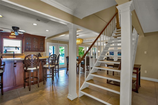 staircase with tile patterned flooring, ceiling fan, ornate columns, and ornamental molding