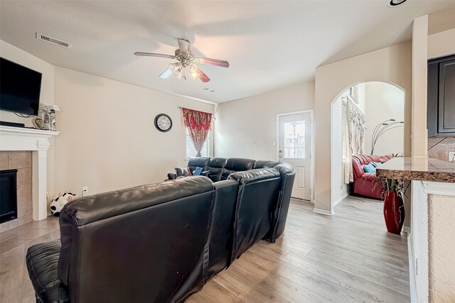 living room with a fireplace, ceiling fan, and light wood-type flooring