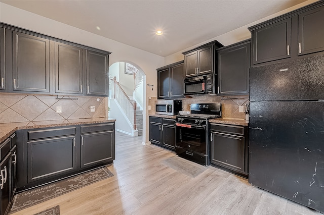 kitchen with light hardwood / wood-style floors, black appliances, stone counters, and backsplash