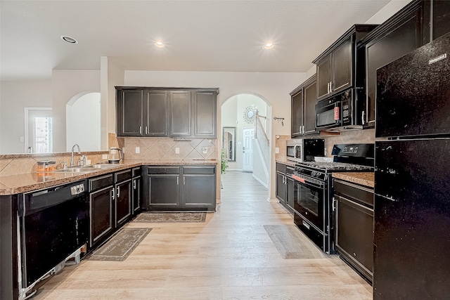 kitchen featuring sink, black appliances, light stone counters, light hardwood / wood-style flooring, and decorative backsplash